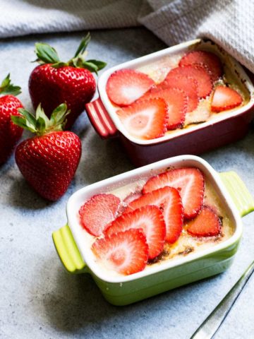 Two ramkeins filled with Keto creme brulee. Three large strawberries to the side.