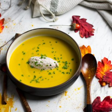 overhead image of bowl of butternut squash bisque with fall leaves decor and wooden spoon