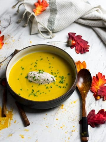overhead image of bowl of butternut squash bisque with fall leaves decor and wooden spoon