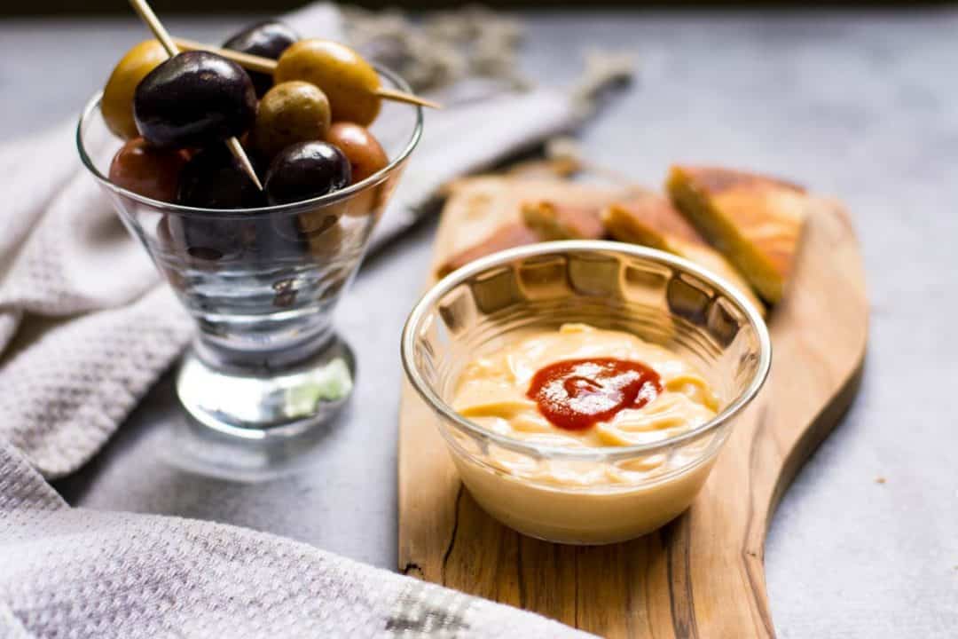 Small bowl of aioli on a wood platter with toast points. Spicy Sriracha Aioli